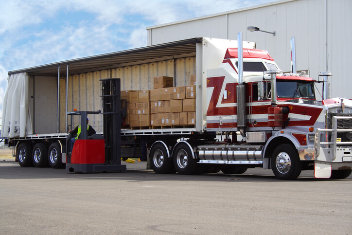 forklift beside a curtain-side truck carrying palletised boxes.